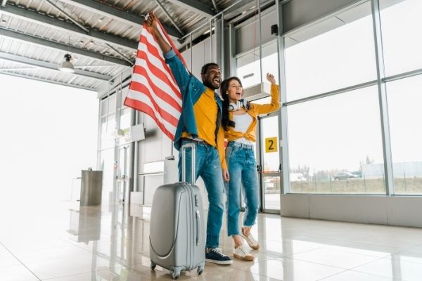 Man and woman standing with suitcase at airport happily waving US flag