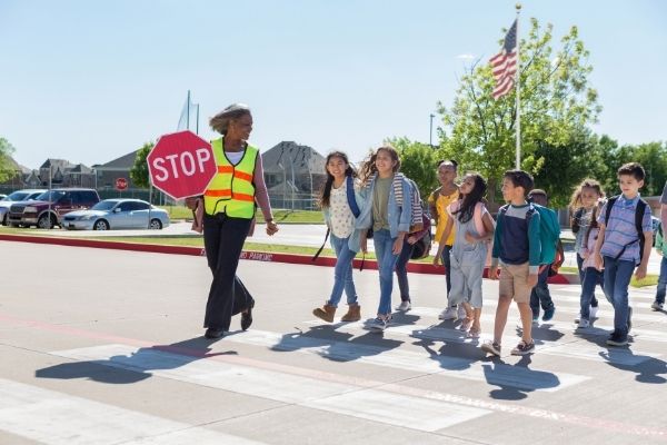  A crossing guard smiles as she walks through a crosswalk with some children