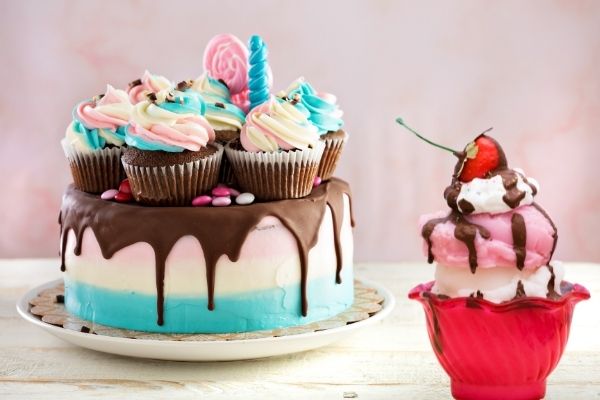 A colorful American cake with various cupcakes stands next to an ice cream sundae